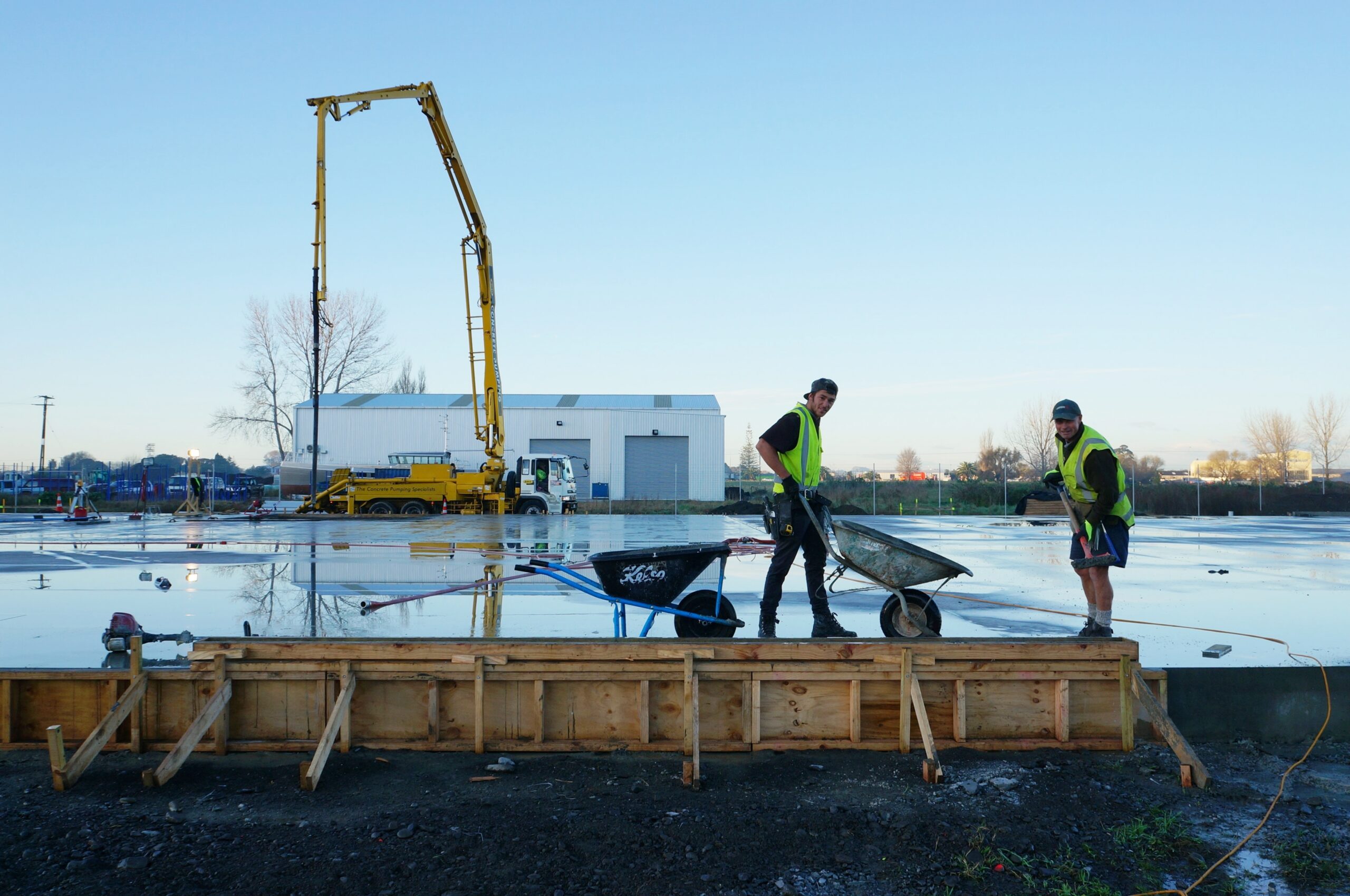 Two tradesmen working on a construction site with wheelbarrows on a concrete pad.